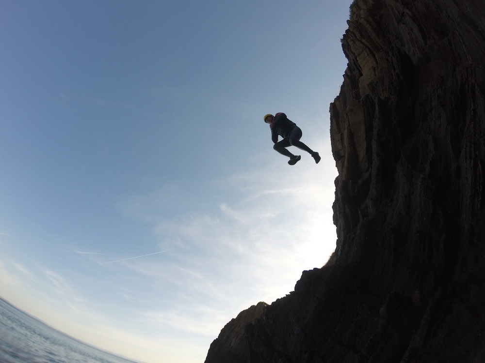 person jumping off cliff coasteering