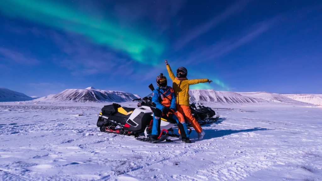 tourists on snowmobile under northern lights