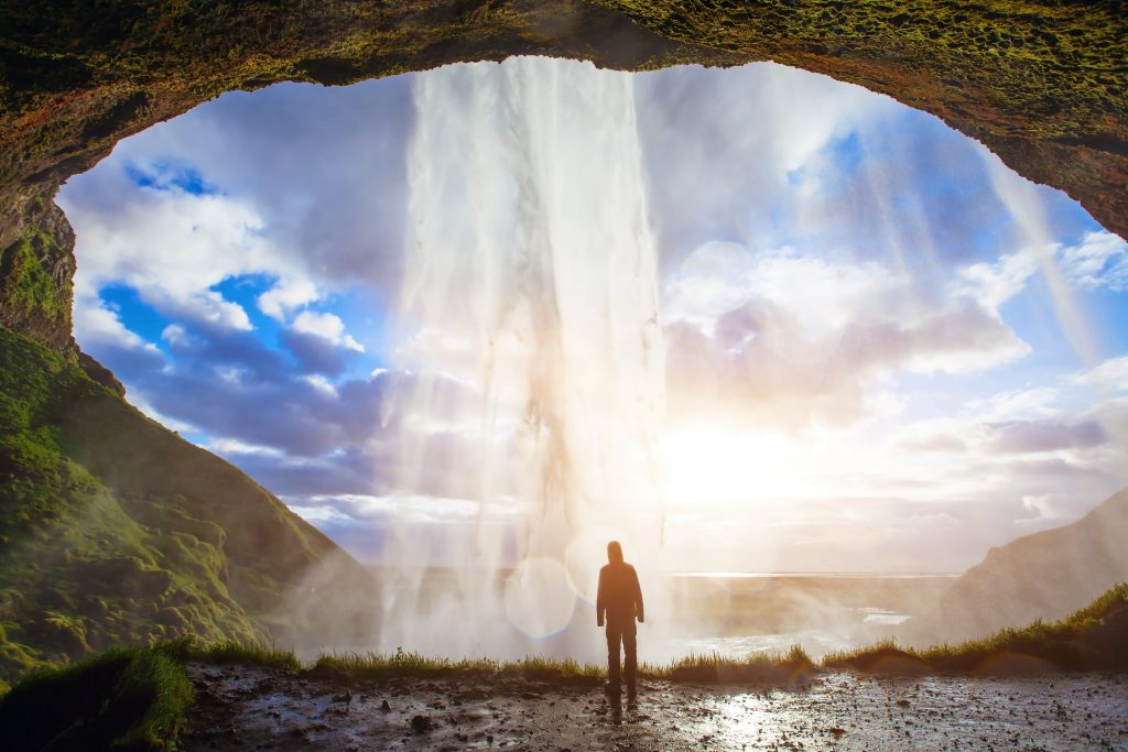 person standing behind a waterfall in iceland